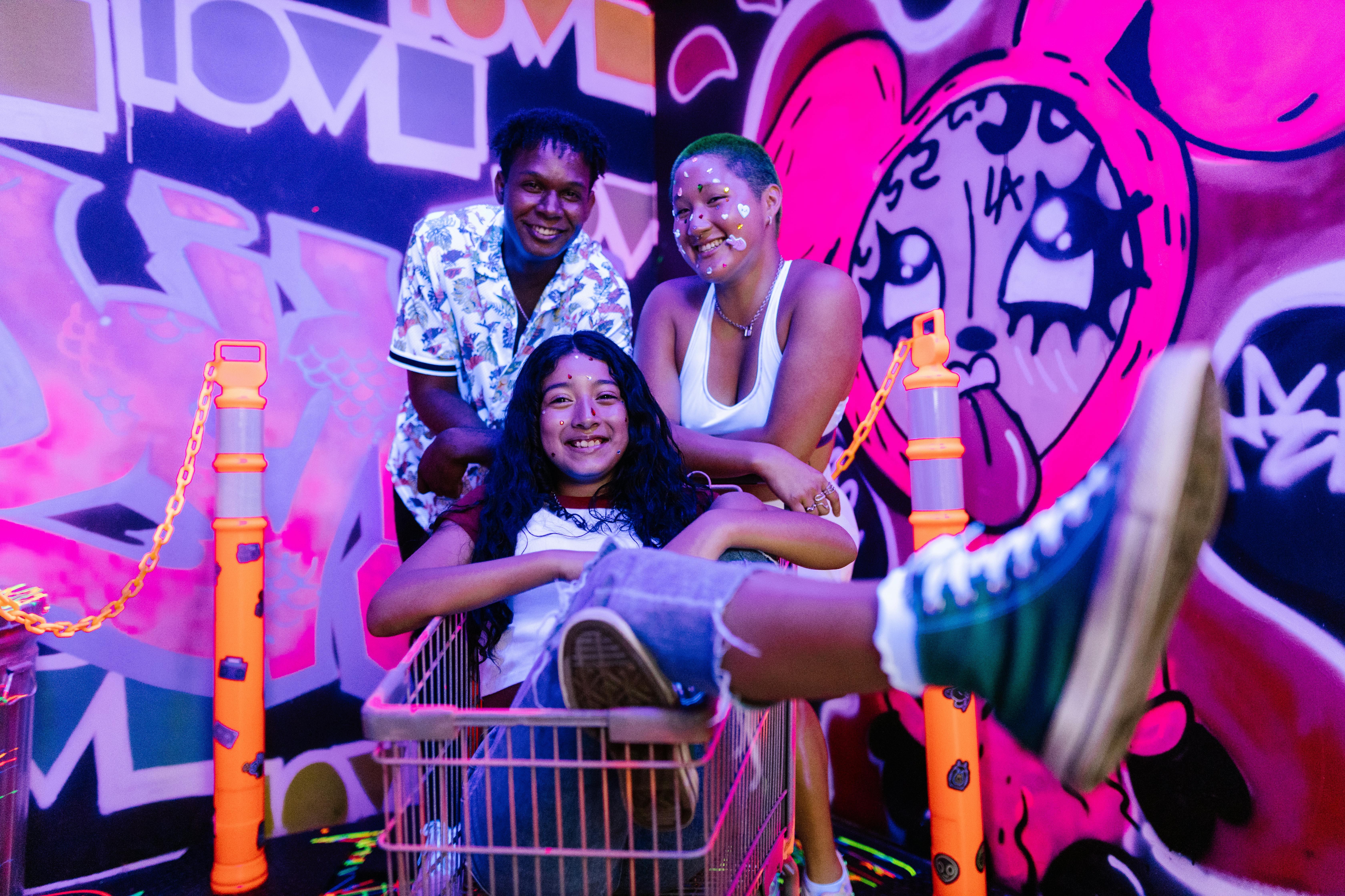 Three friends enjoy a fun moment in a shopping cart against vivid graffiti.