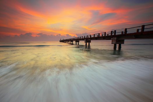 日出时分，海浪拍打码头，天空色彩缤纷，景色迷人