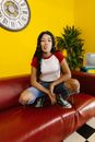 Woman in White Tank Top and Blue Denim Jeans Sitting on Red Couch