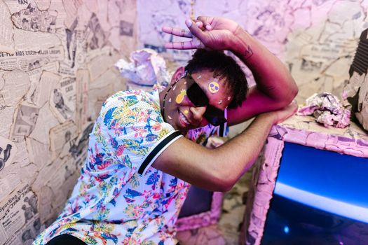 Fashionable man with emoji stickers and sunglasses posing playfully in a retro-inspired room.