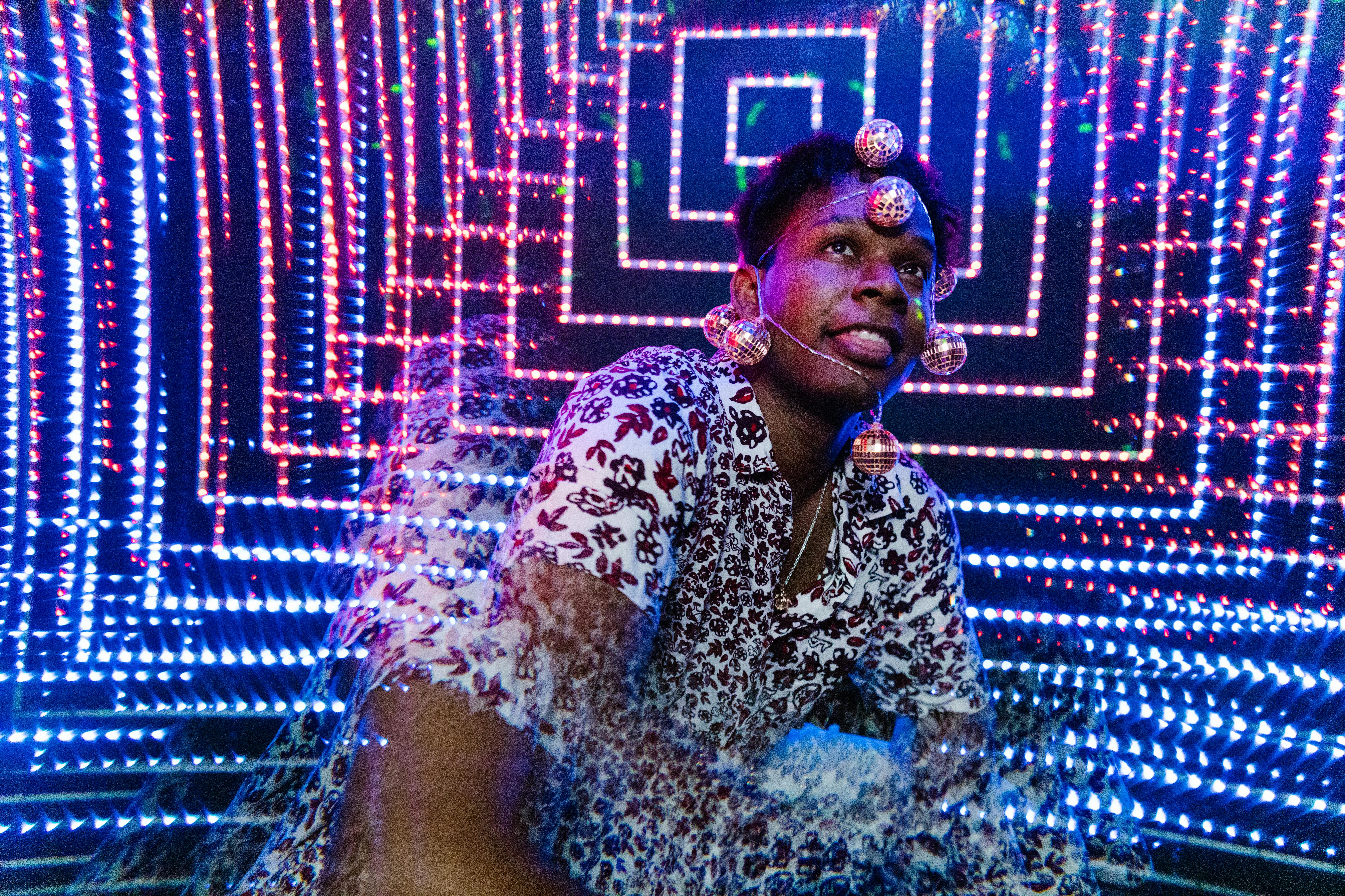 A man wearing reflective orbs poses amidst festive blue and red LED lights.