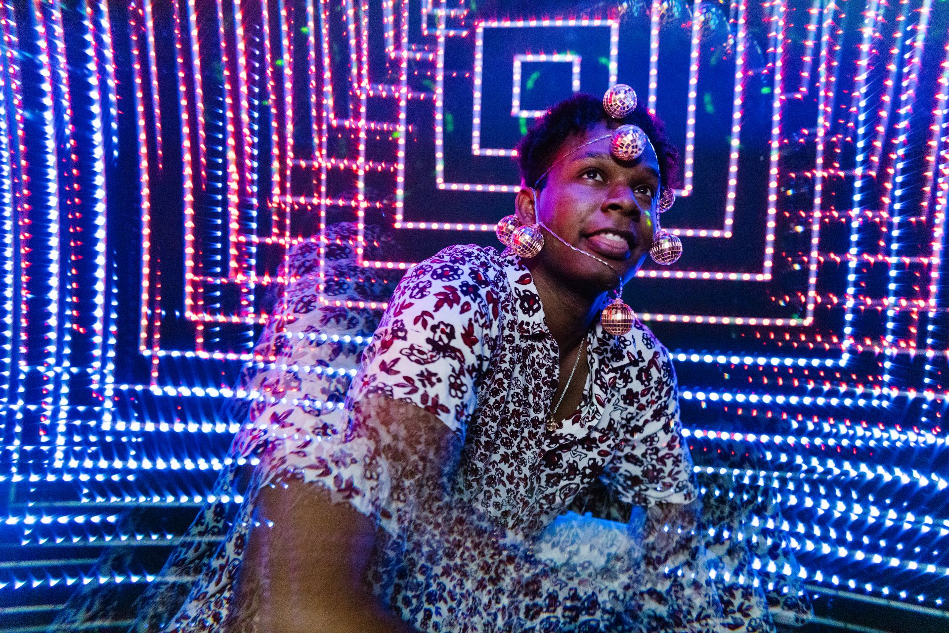 A man wearing reflective orbs poses amidst festive blue and red LED lights.
