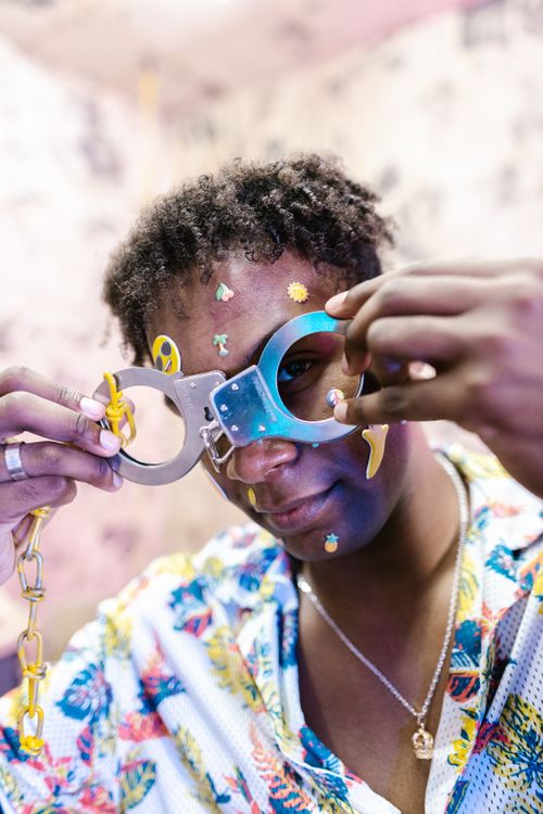 Free Young adult playfully poses with novelty handcuffs, decorated with stickers, in a vibrant setting. Stock Photo