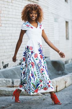 African American woman in a colorful floral dress walking confidently outdoors.