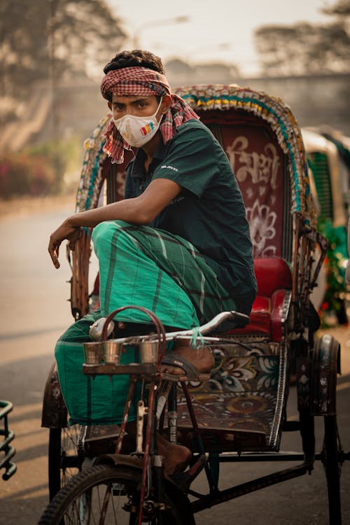 Man in Green Shirt and Pants Riding a Rickshaw