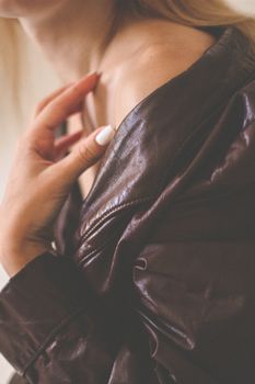 A woman lightly touches her shoulder while wearing a brown leather jacket, showcasing a manicure.
