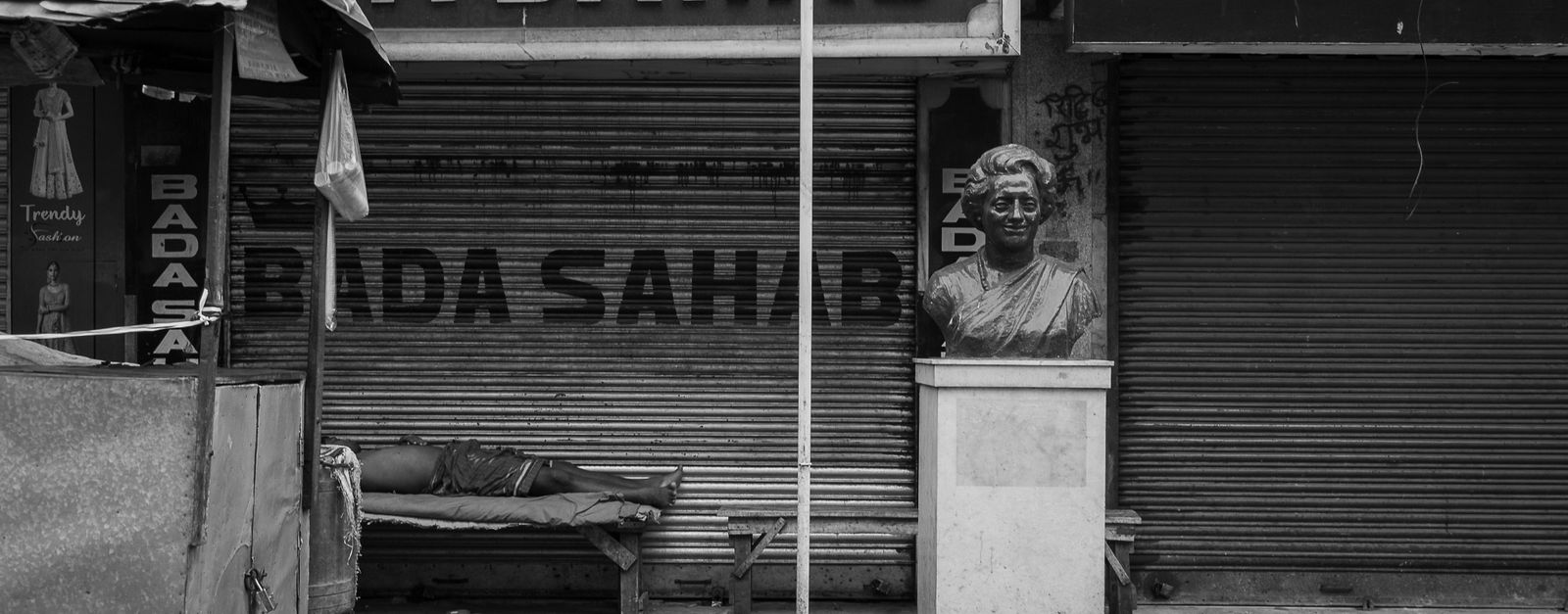Monochrome photo of a city street showing a bust statue and closed shop.