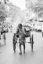 Grayscale Photo of Man Pulling a Rickshaw