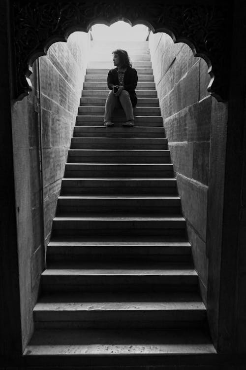 Monochrome Photo of Person Sitting Alone on the Staircase