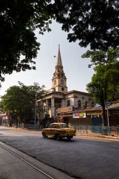 A classic view of a Kolkata street featuring a historic church and a vintage car in daylight.