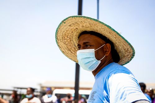 Free A man in a blue shirt and straw hat wearing a face mask in a public outdoor area. Stock Photo