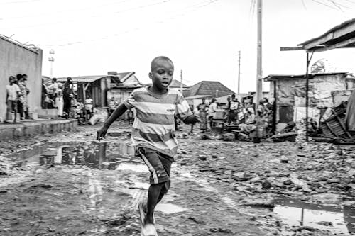 Grayscale Photo of Boy Running on the Muddy Ground 