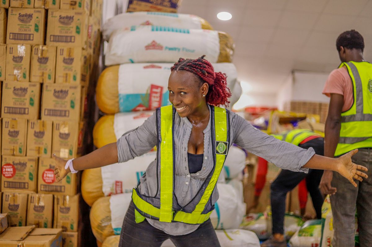 Joyful female worker in a warehouse surrounded by stacked goods, wearing a safety vest.