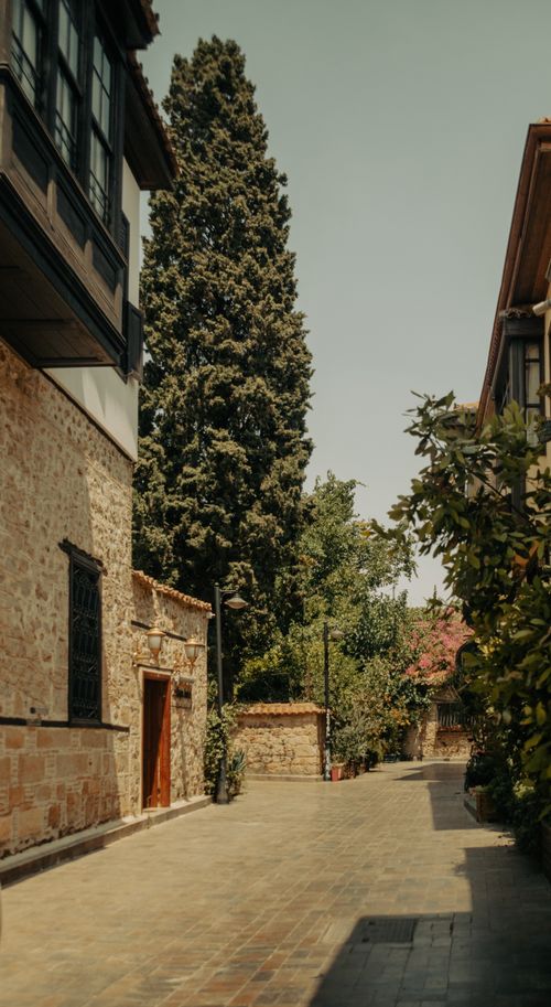 Free Scenic alleyway lined with stone buildings and lush greenery under a clear sky. Stock Photo