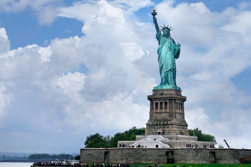 Free Iconic Statue of Liberty on Liberty Island, New York, with a cloudy sky backdrop. Stock Photo