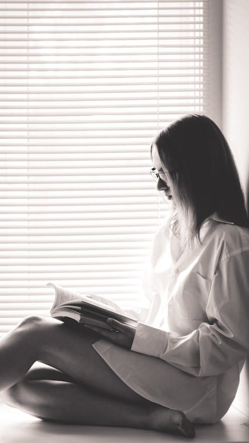 Free 
A Grayscale of a Woman Reading a Book by the Window Stock Photo