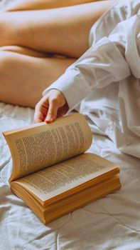 Close-up of a person flipping pages of a book on a bed, wearing a white shirt in a warm, cozy environment.