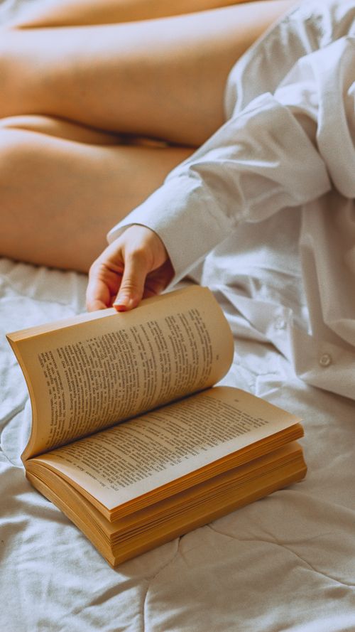Free Close-up of a person flipping pages of a book on a bed, wearing a white shirt in a warm, cozy environment. Stock Photo