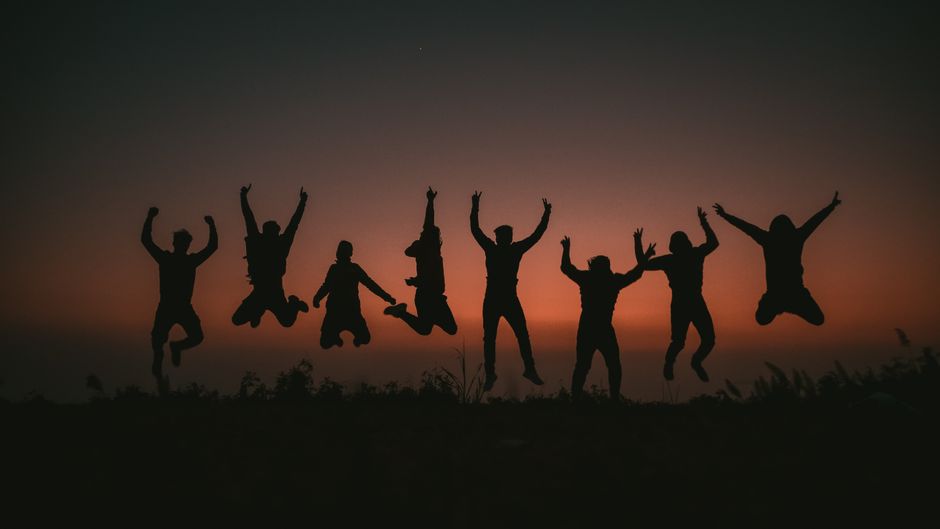 A group of friends silhouetted against a vivid sunset, jumping in the air.