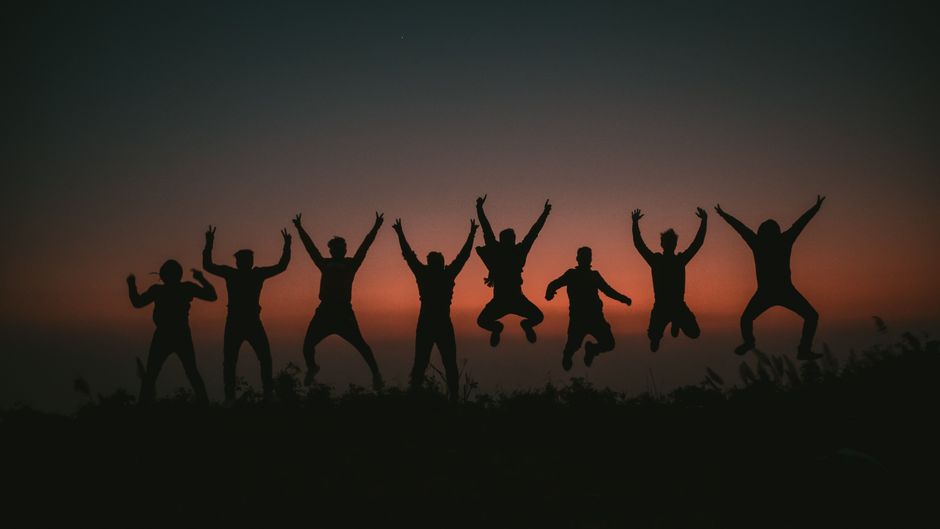 A group of people joyfully jumping against a colorful sunset, creating dramatic silhouettes.
