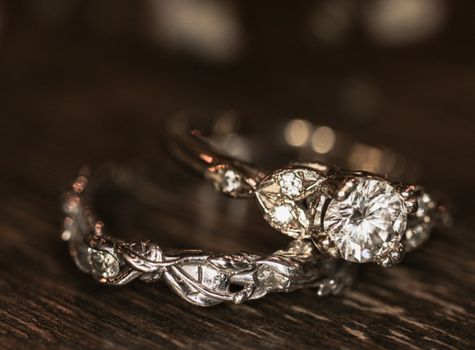 Close-up of elegant silver engagement and wedding rings with diamonds on a wooden surface.