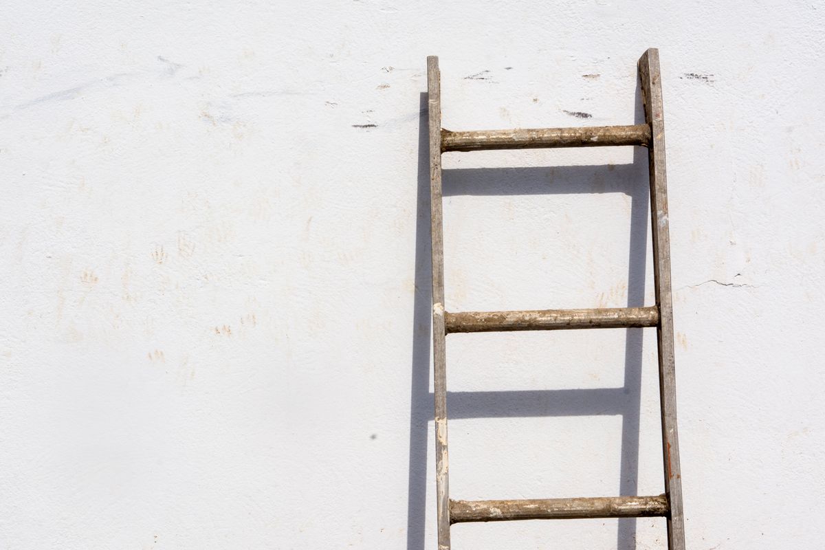 Wooden ladder leaning against a weathered white concrete wall in natural light