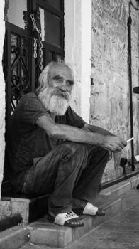 Black and white portrait of an elderly man sitting on steps in an urban street setting.