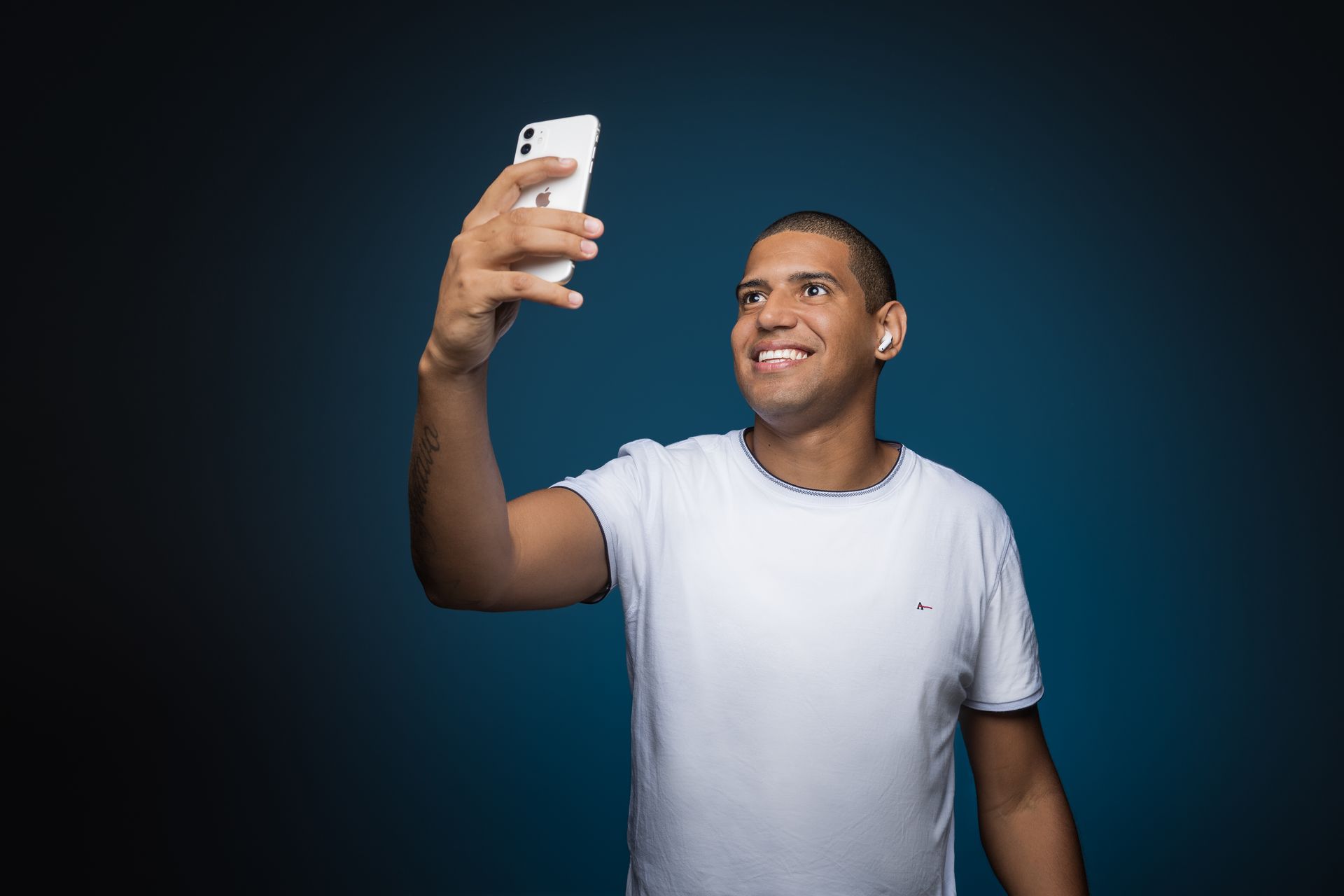 A cheerful man in a white shirt taking a selfie with his smartphone.