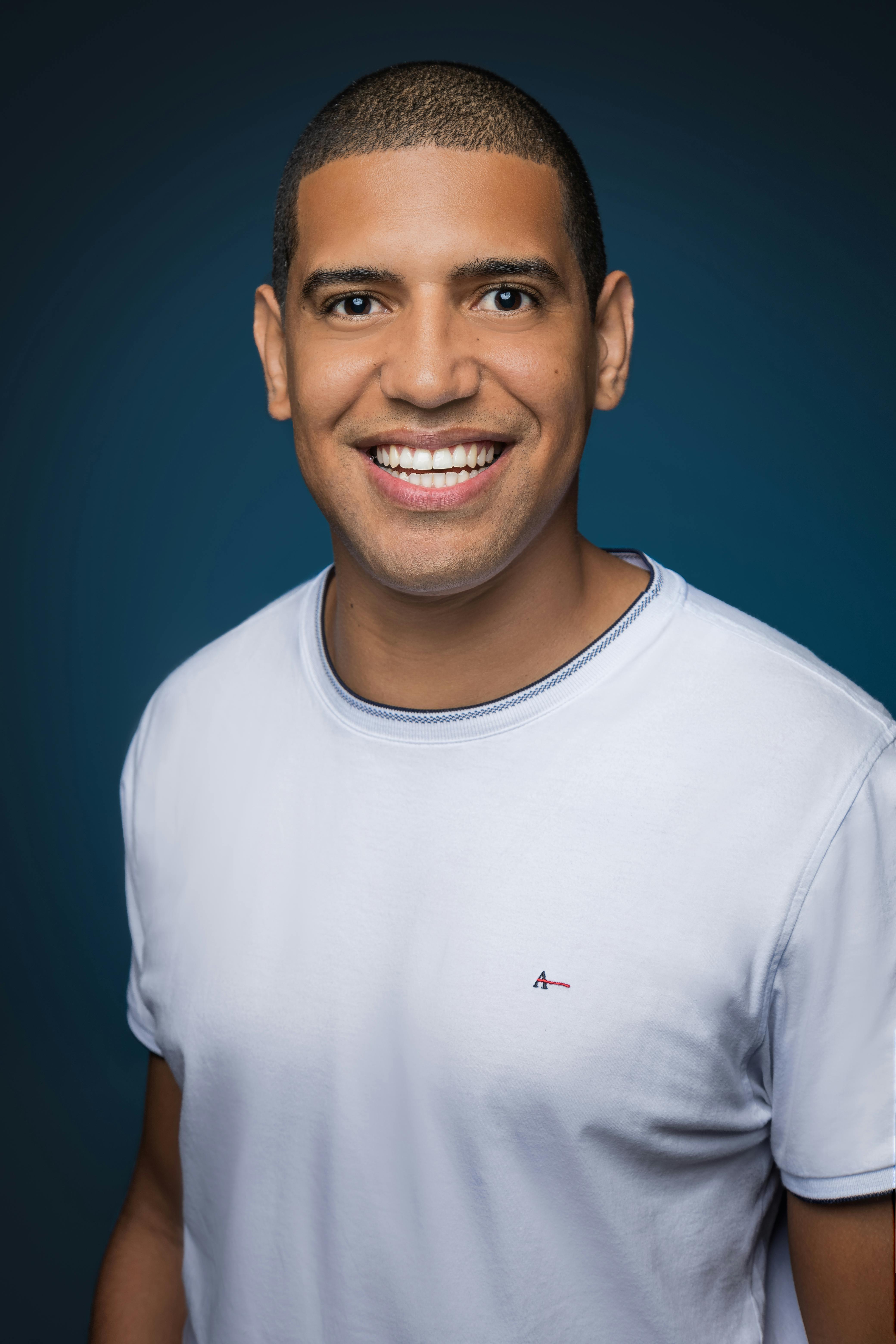 Smiling man in a white shirt against a blue background, exuding warmth and confidence.