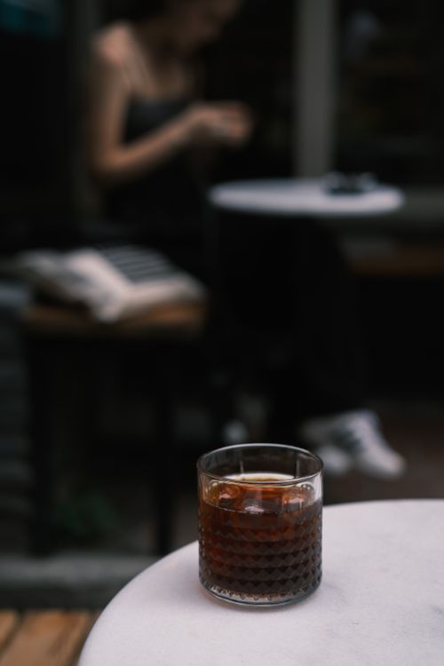 Free A moody, close-up shot of a cold brew coffee glass on a cafe table with blurred background. Stock Photo