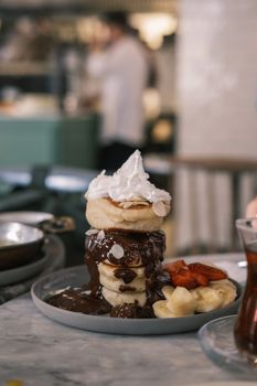 Indulgent pancake stack topped with chocolate sauce, whipped cream, and fresh fruit, perfect for dessert lovers.