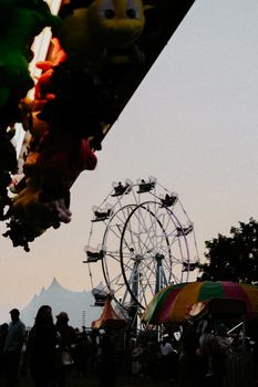 Ferris wheel against a twilight sky at a lively carnival with silhouetted visitors.