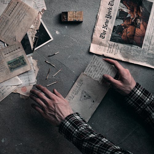 Free From above of crop unrecognizable man opening and reading old letters on gray surface with newspaper and matches Stock Photo