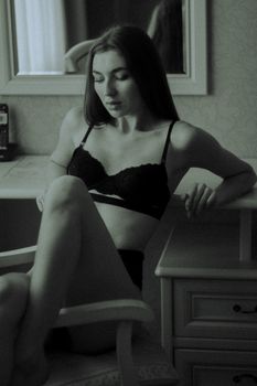 A stylish monochrome portrait featuring a woman in lingerie sitting at an indoor setting.