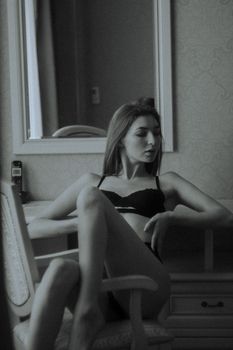 Sophisticated monochrome portrait of a woman in lingerie sitting by a mirror indoors.