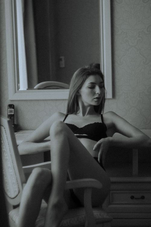 Free Sophisticated monochrome portrait of a woman in lingerie sitting by a mirror indoors. Stock Photo