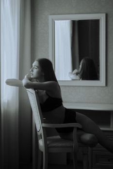 Elegant black and white portrait of a woman in lingerie sitting by a window, captured in a reflective mood.