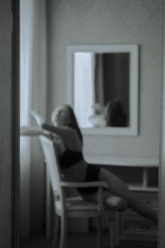 Moody black and white portrait of a woman in lingerie by the window.