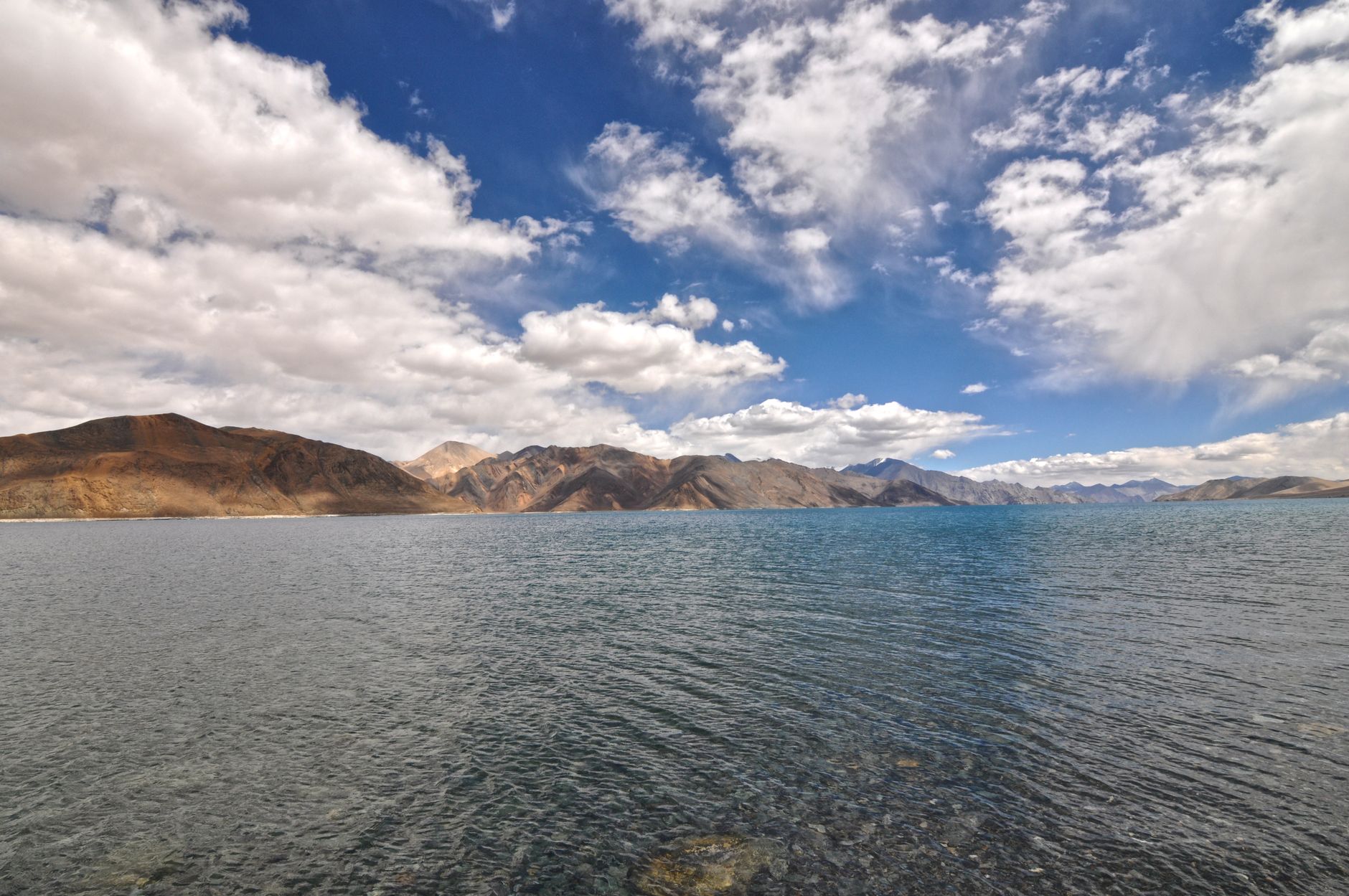 A breathtaking landscape of Pangong Lake with clear skies and surrounding mountains, offering a serene nature scene.