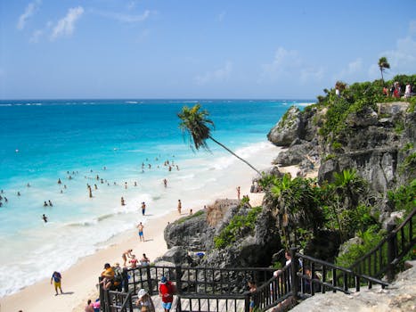 Crowded beach with turquoise water and rocky cliffs under a bright sky.