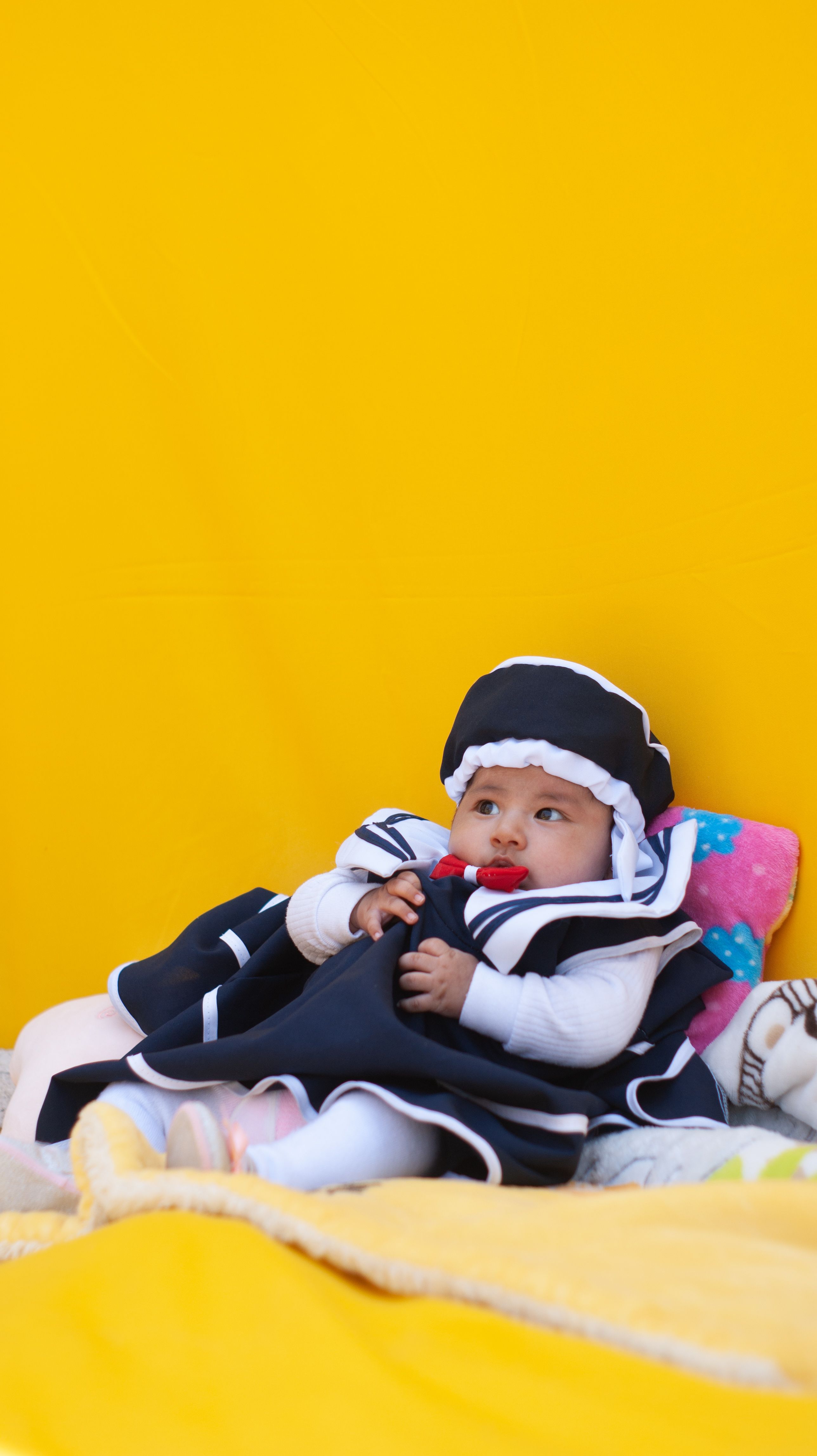 Bebê adorável vestido com roupa de marinheiro deitado em cobertores coloridos com um fundo vibrante amarelo.