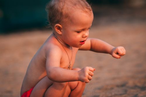 Free A young child playing with sand, capturing a moment of curiosity and innocence at the beach during golden hour. Stock Photo
