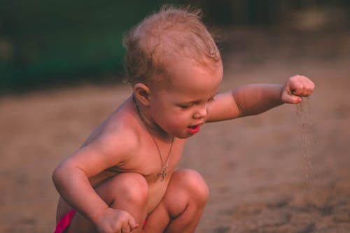 昼間に砂を保持しているペンダントネックレスを持つ赤ちゃん