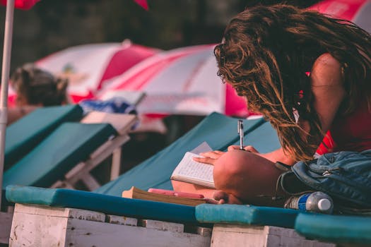 一名年轻女子坐在沙滩椅上，在遮阳伞下用笔记本写字