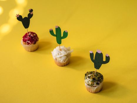 Three decorative cupcakes with cactus toppers on a vibrant yellow background, perfect for festive occasions.