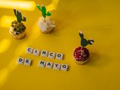 Festive cupcakes and scrabble tiles on a bright yellow background celebrating Cinco de Mayo.