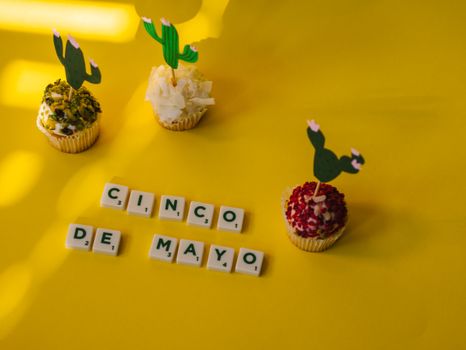 Festive cupcakes and scrabble tiles on a bright yellow background celebrating Cinco de Mayo.