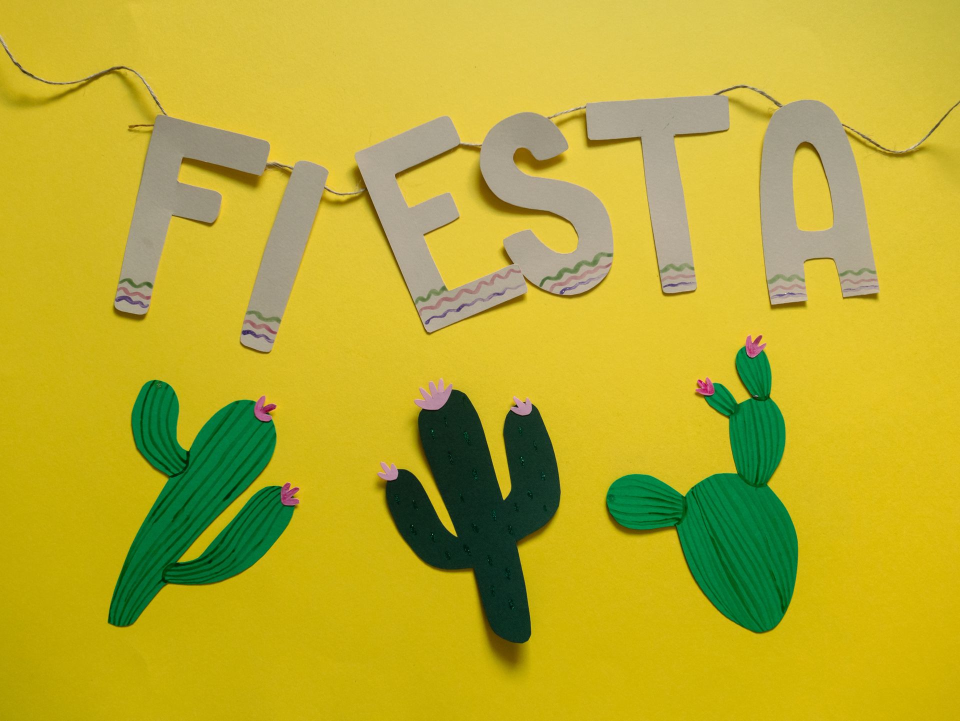 Festive decoration for a fiesta with vibrant cactus paper cutouts on a yellow background.