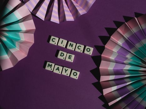 Cinco de Mayo celebration layout with fan decorations and letter tiles on a purple surface.