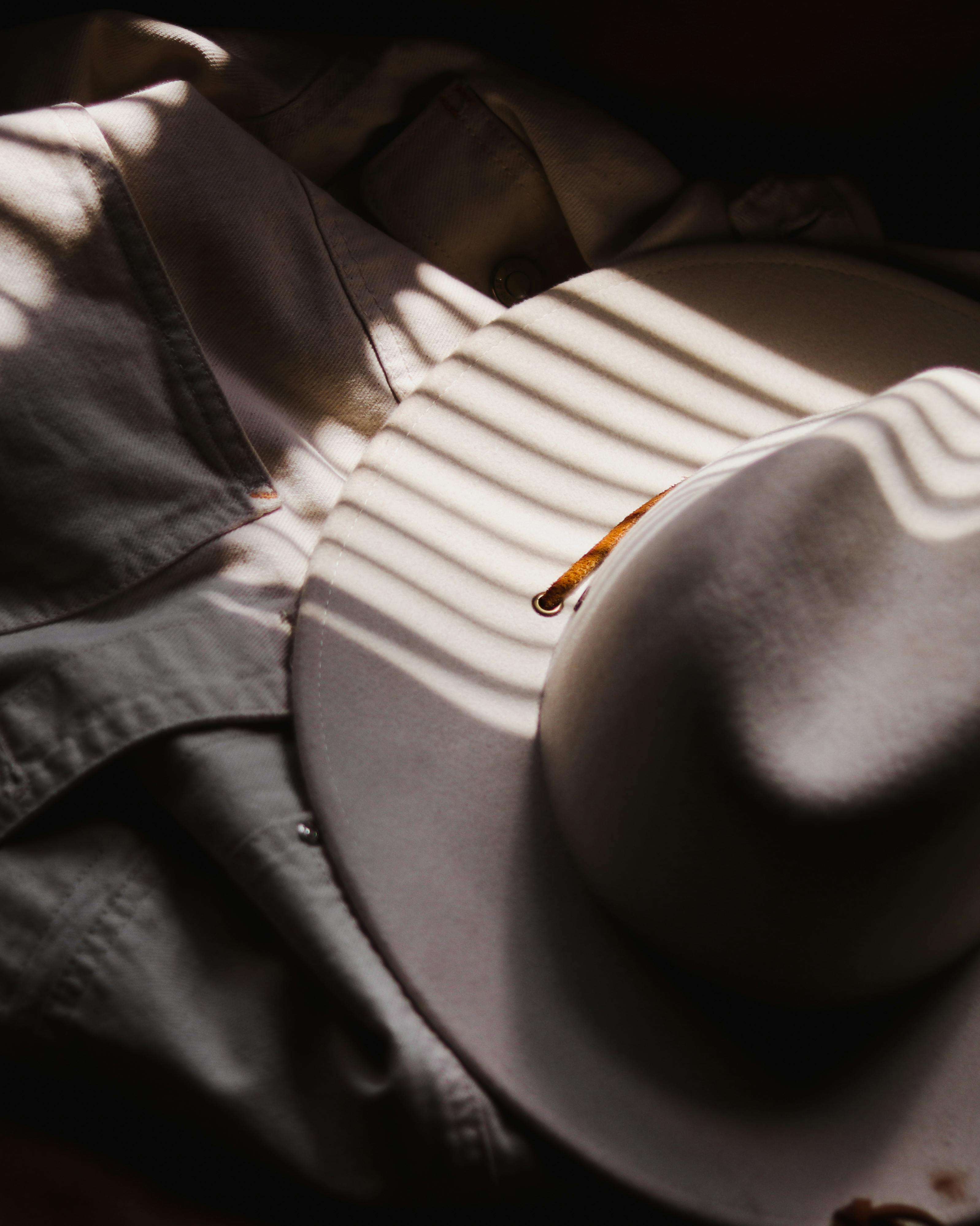 A classic fedora hat casts shadows on a denim jacket with artistic lighting.